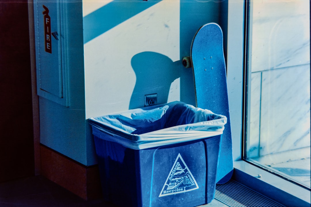 Blue trash can and skateboard by a window