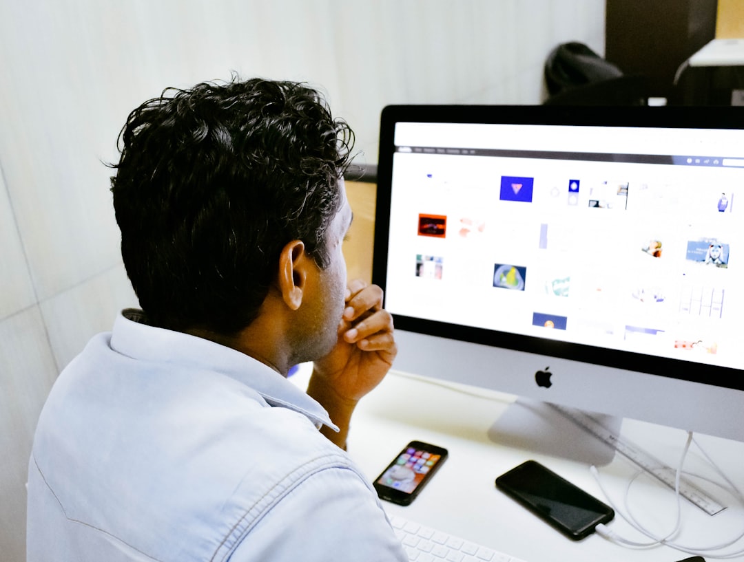 man sitting in front of silver Apple iMac on table