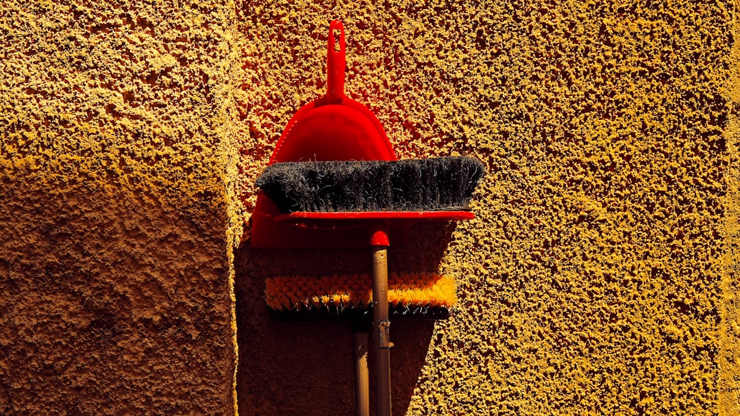 Red dustpan and broom leaning against wall