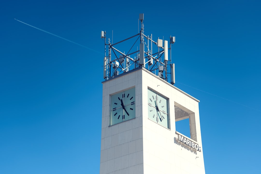 White tower with clock faces and antennas against blue sky