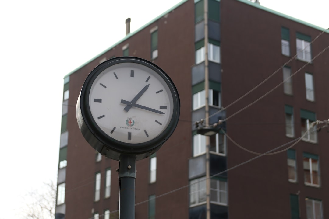 A clock stands in front of a brick building.