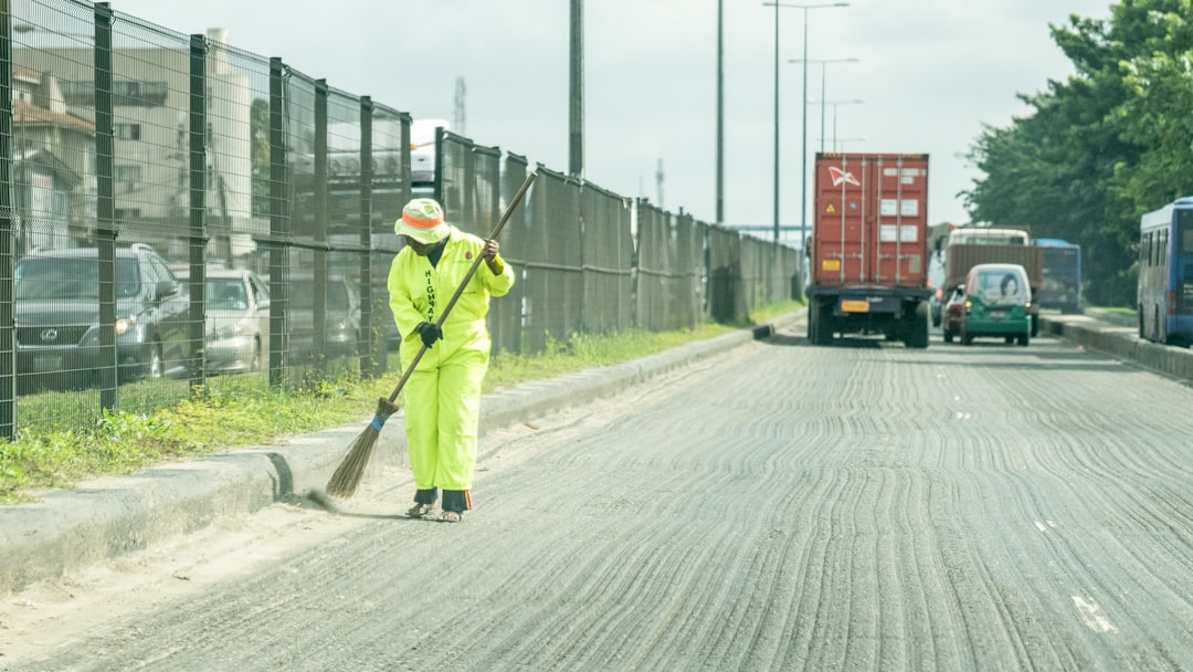 man in green jacket and green pants holding shovel walking on road during daytime