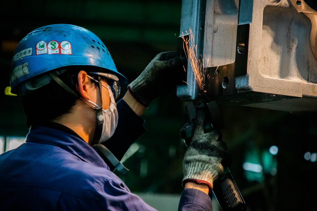 man in blue jacket and red helmet holding black and orange power tool