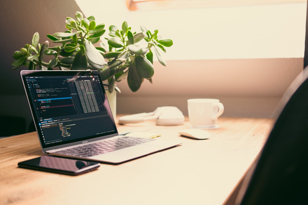 Laptop with code, plant, and coffee cup on desk.
