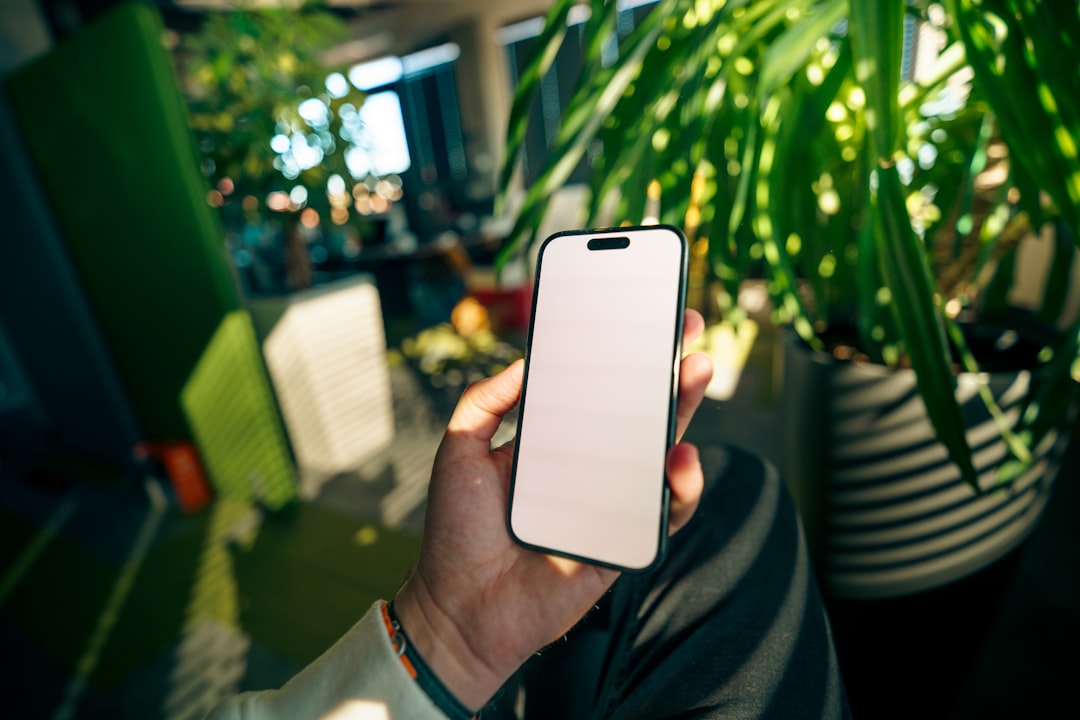 Hand holding a smartphone with blank screen indoors.
