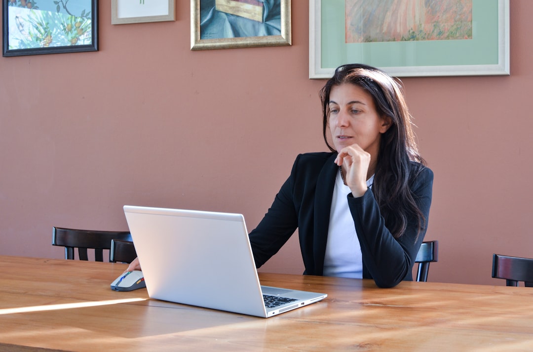 Woman in a black blazer working on a laptop.
