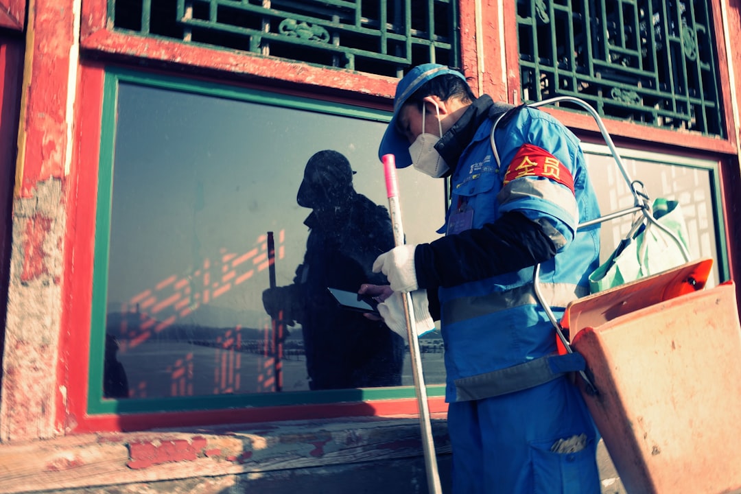 Worker in blue uniform cleans window with spray bottle
